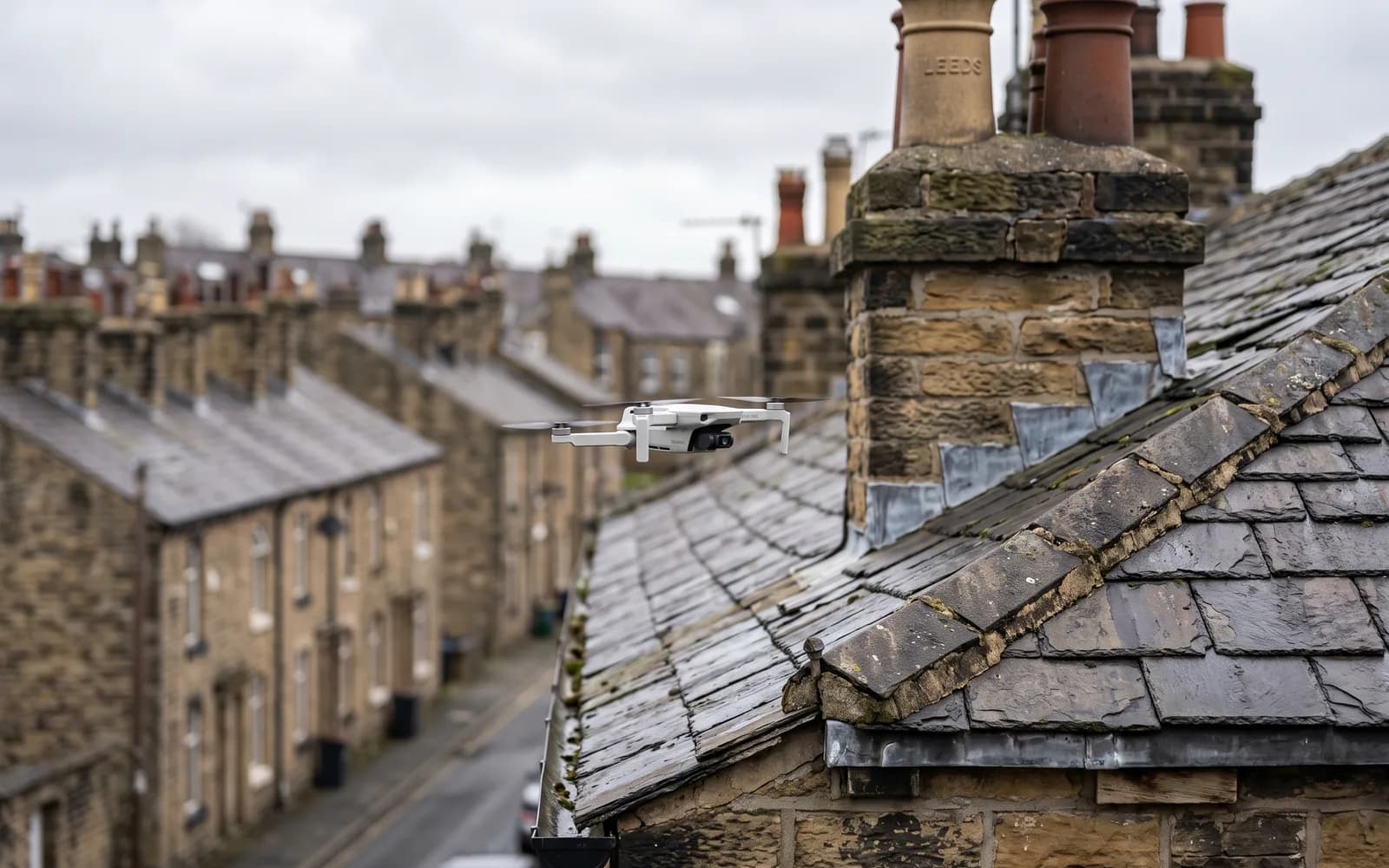 A drone inspecting the slate roofline and chimney stacks of a row of Yorkshire stone terraced houses in Leeds